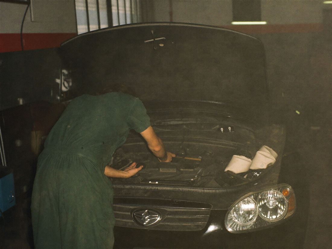 Mechanik pochylony nad otwartą maską samochodu w warsztacie
